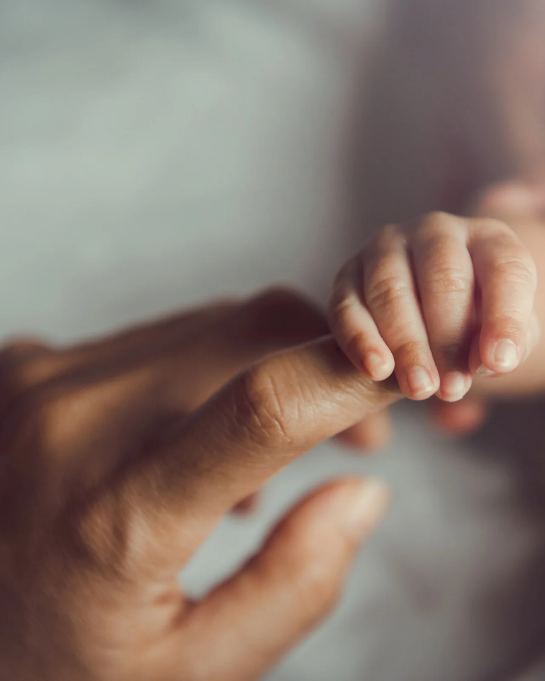 Newborn baby holding an adult’s finger.