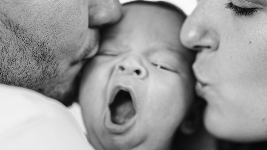 Black white photo pf newborn with parents kissing them. 