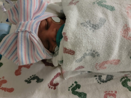 Premature newborn baby resting in the NICU, wearing a striped hospital hat and wrapped in a blanket while receiving respiratory support.