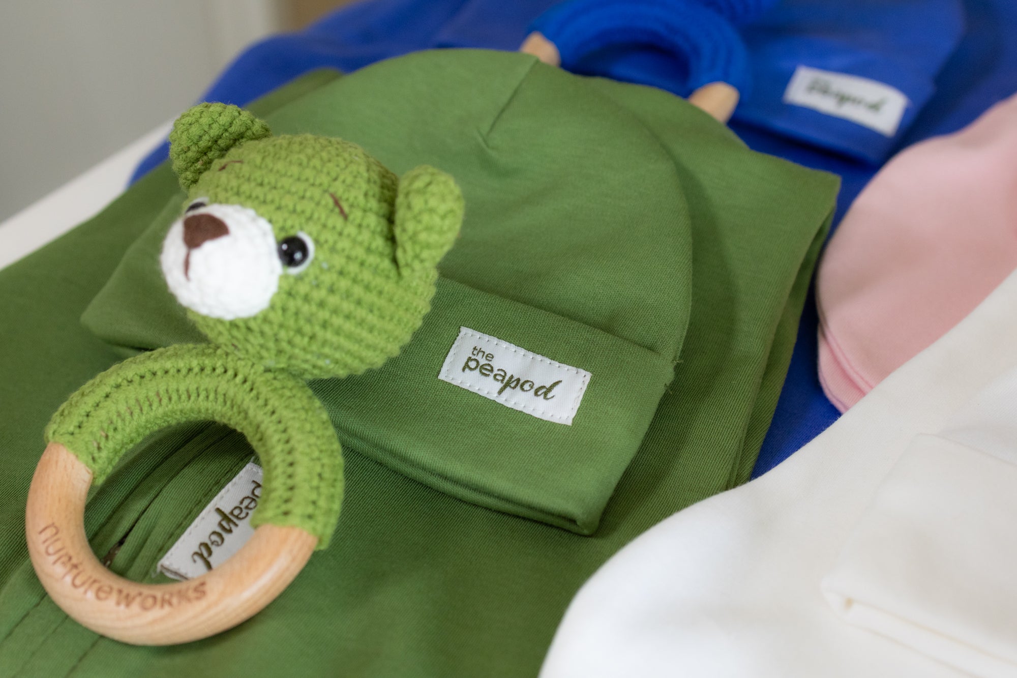 Green baby sleep sack with matching hat and crochet bear rattle laid out on a surface.