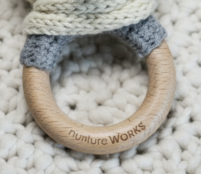 Wooden teething ring with 'nurture WORKS' engraving on a textured surface