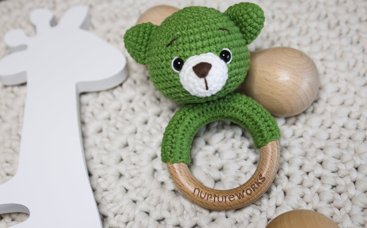 Green crochet bear rattle with a wooden ring.