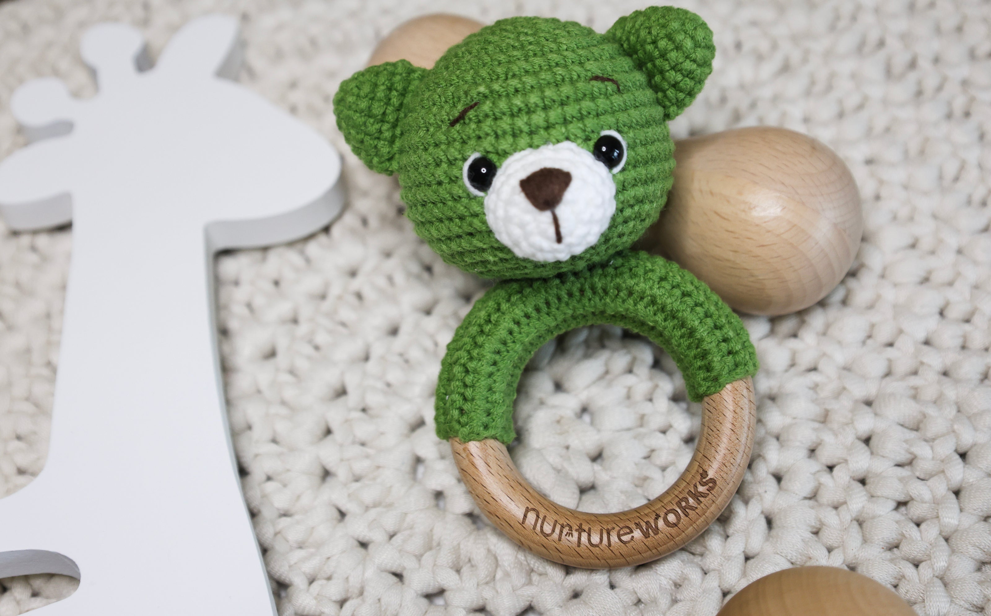 Green crochet bear rattle with a wooden ring.