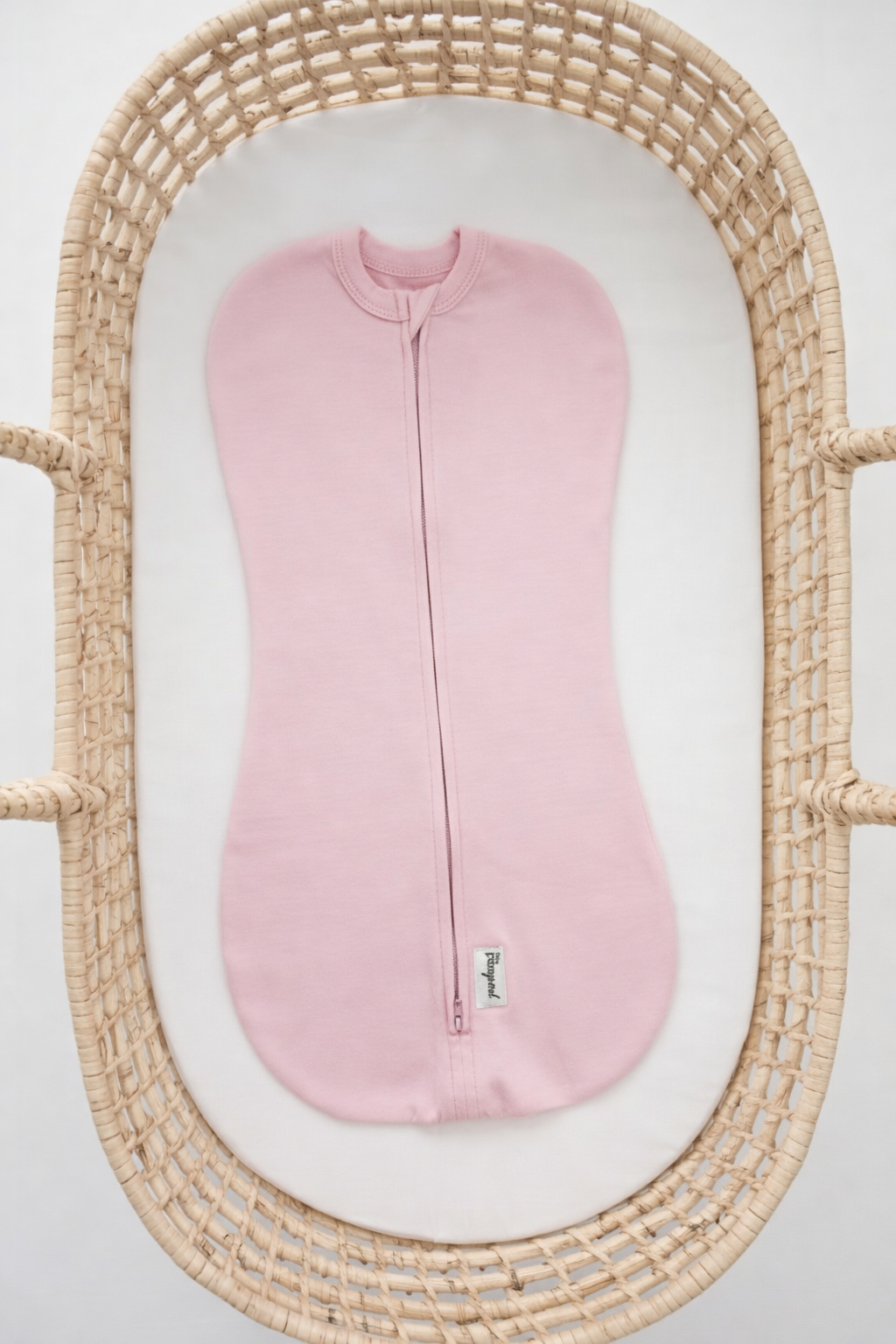 Pink baby swaddle sleep sack in a wicker bassinet on a light gray background