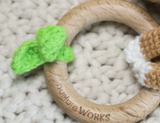 Wooden teething ring with green leaf on a textured surface
