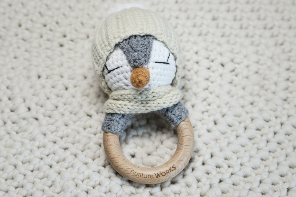 penguin crochet rattle with a wooden ring on a textured blanket