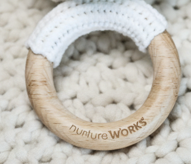 Wooden teething ring with 'nurture works' branding on a textured surface